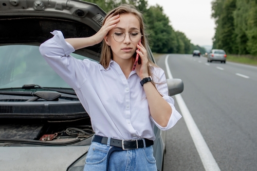 Young,Woman,Standing,Near,Broken,Down,Car,With,Popped,Up